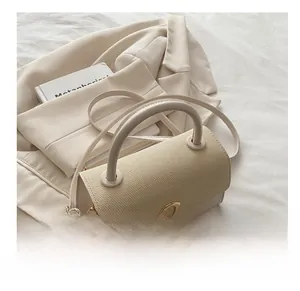 Detail view of beige textured handbag with gold triangular clasp and soft tubular handle