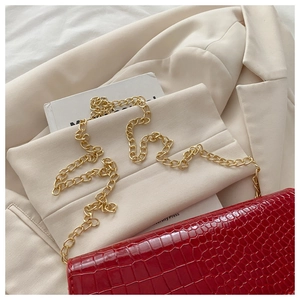 Detailed view of red crocodile-pattern leather handbag with golden metal chain strap