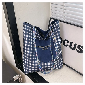 Detailed close-up of blue plaid canvas tote bag with embroidered denim front pocket
