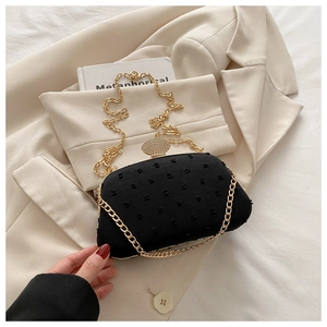 Detail of black polka dot evening clutch with gold chain on a beige blazer background