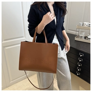 Detail shot of large brown leather tote bag showing handle attachments and embossed text