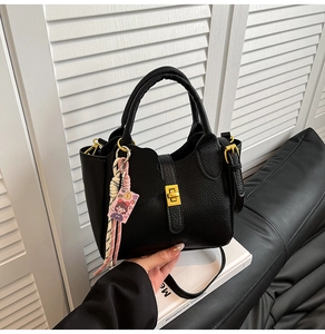 Close-up of a minimalist black lychee grain handbag with gold hardware and cute pink charm