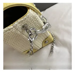 Close-up of silver metal chain hook and spring buckle on yellow woven crossbody bag