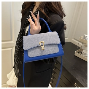 Blue leather bag with striped flap and gold horseshoe lock shown in a lifestyle setting