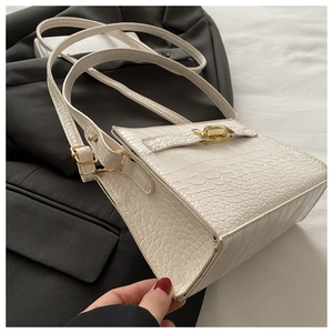 Detail of white crocodile embossed crossbody bag featuring a golden twist lock closure