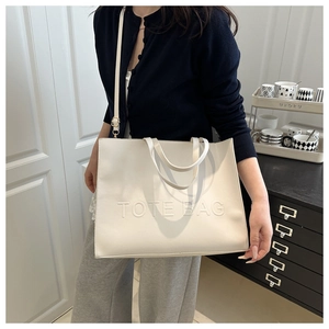 Detail of cream white tote bag featuring embossed TOTE BAG text and adjustable strap
