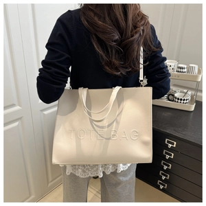Detail of cream tote bag featuring embossed logo and textured faux leather shoulder strap