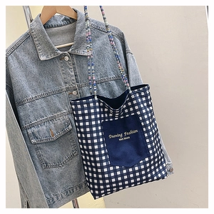 Detailed close-up of a blue plaid canvas tote featuring gold embroidery and beaded handle