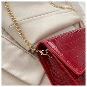 Close-up of red patent leather crocodile pattern texture and gold chain on the shoulder bag
