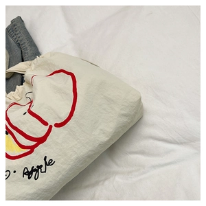 Detailed close-up of cream nylon tote bag featuring artistic red apple print and text