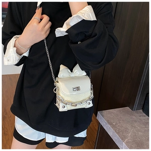 Detail of cream mini crossbody bag with oversized bow and woven texture on model
