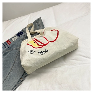 Detail of cream canvas tote bag with red hand-drawn apple pattern and soft drawstring top
