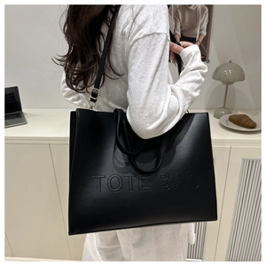 Close-up of black tote bag with embossed TOTE BAG text and golden metal buckles