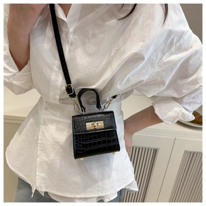 Detail of black crocodile texture mini handbag with gold twist lock on a model