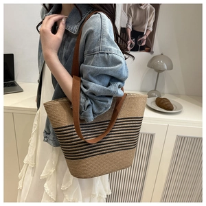 Detail of a large khaki straw tote bag with black stripes and brown fabric shoulder straps