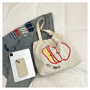 Macro detail of the cream nylon tote with artistic apple print and drawstring closure