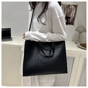 Detailed close-up of a black matte leather tote bag with embossed TOTE BAG letters
