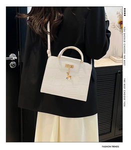 Detail of white minimalist handbag with gold ring handle and metal deer charm decoration