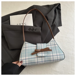 Detail of blue plaid underarm bag with a brown bow and leather strap on a textured surface