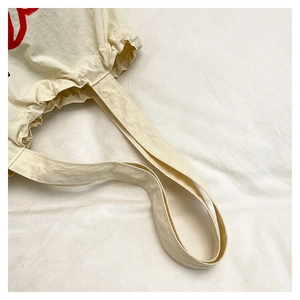 Detail of off-white nylon tote bag showing crinkled texture and wide shoulder strap