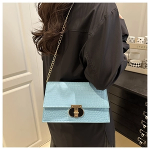 Detail of light blue crocodile texture handbag with gold T-shaped lock and chain strap
