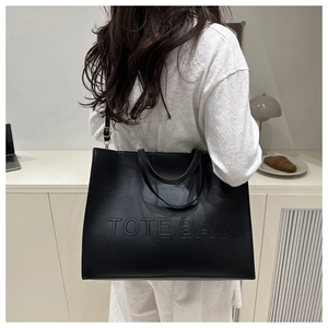 Detail of black leather tote bag with embossed lettering and adjustable shoulder strap