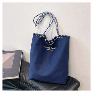 Close-up of embroidered canvas tote bag with woven handles and checkered lining