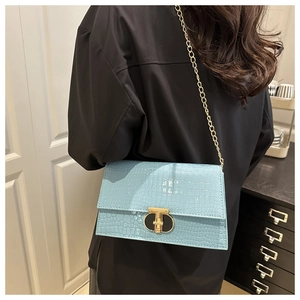 Detail of light blue crocodile pattern texture and golden T-shaped metal clasp on bag