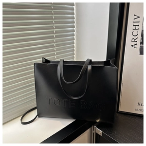 Detail of embossed TOTE BAG lettering on a textured black leather tote bag surface