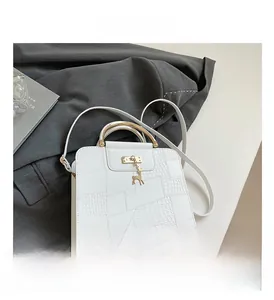 Detail of white crocodile texture bag with gold handle and deer charm on a gray blazer