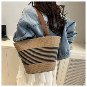 Detailed view of woven straw tote bag featuring horizontal black stripes and brown straps