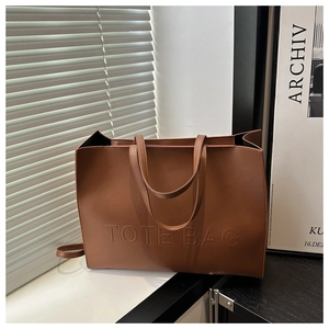 Detail of embossed TOTE BAG lettering on large brown leather shoulder bag