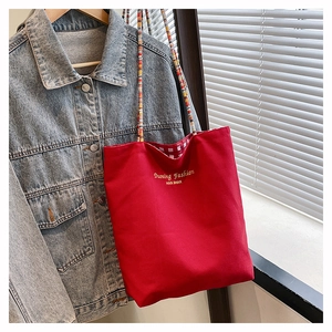 Detail of a red canvas tote bag with embroidered letters and a colorful beaded strap