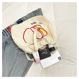Flat lay of cream nylon tote bag with red apple print, books, and tablet for daily use