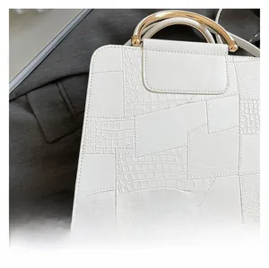 Detail of white crocodile pattern PU handbag with metallic handle and textured paneling