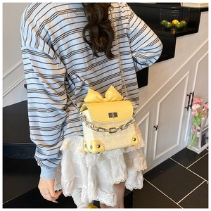 Detail view of a yellow woven crossbody bag with large bow and silver chain strap