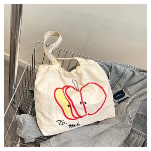 Detail of off-white nylon tote bag with red apple print and drawstring in a lifestyle setting
