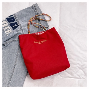 Detail of red canvas tote bag featuring colorful woven rope handles and checkered lining