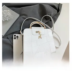 Close-up of white croc-textured handbag with gold curved handle and deer charm