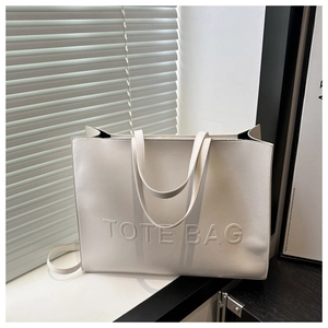 Detail of white tote bag featuring embossed TOTE BAG text and smooth PU leather texture