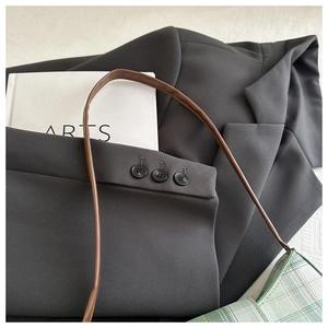 Detailed close-up of blazer sleeve with triple buttons and a green plaid shoulder bag