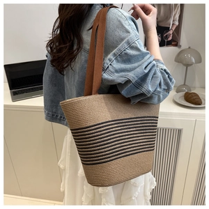 Detail of woven straw tote bag featuring black stripes and brown fabric shoulder straps