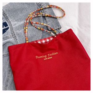 Detail of red canvas tote with woven multicolor handle and plaid lining