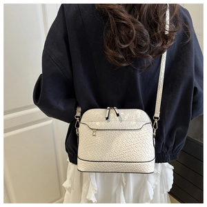 Detail of white shell-shaped crossbody bag with woven texture and gold hardware on model