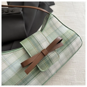 Detail of green and white plaid shoulder bag featuring a brown synthetic leather bow