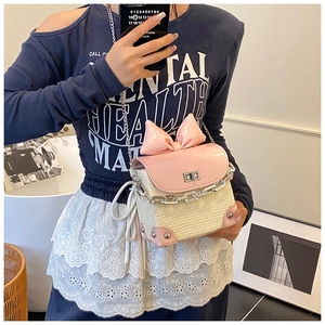 Close-up of woven straw and pink leather crossbody bag with bow and metal chain strap