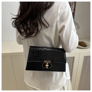 Chic black crocodile pattern crossbody bag with gold lock and chain strap on a model