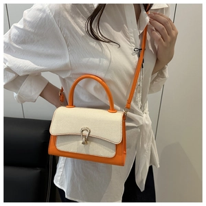 Detail of a chic orange leather crossbody bag with cream woven flap on a white shirt