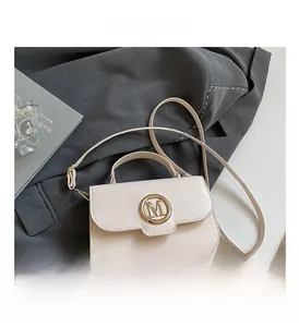 Detail of cream white leather handbag featuring a gold M-shaped metal buckle and strap