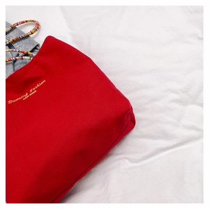 Macro shot of red canvas tote bag showing yellow brand embroidery and cord handle detail